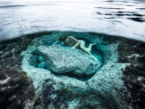 underwater fine art photography - a woman is lying close to an underwater rock showing care for the planet