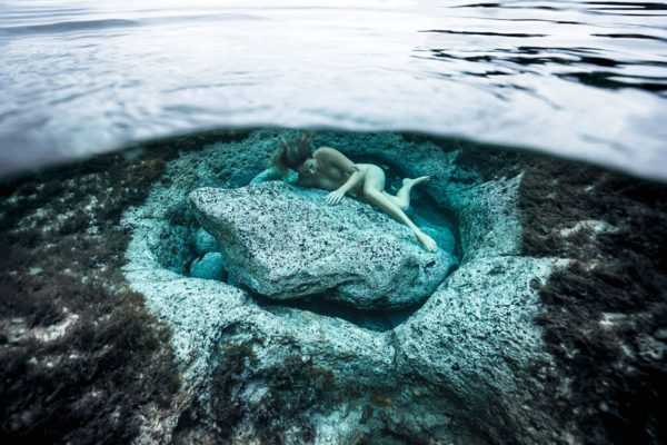 underwater fine art photography - a woman is lying close to an underwater rock showing care for the planet