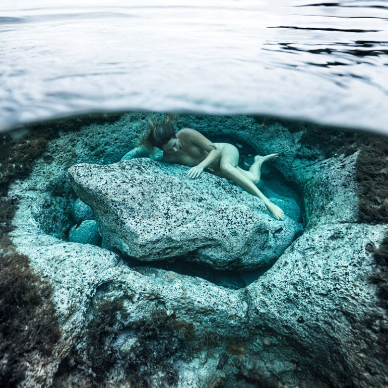 underwater fine art photography - a woman is lying close to an underwater rock showing care for the planet