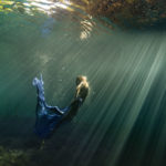 femme sous l'eau dans un bassin naturel sur l'île de La Réunion, lors d'une séance artistique sous l'eau. Elle est entourée des rayons du soleil.
