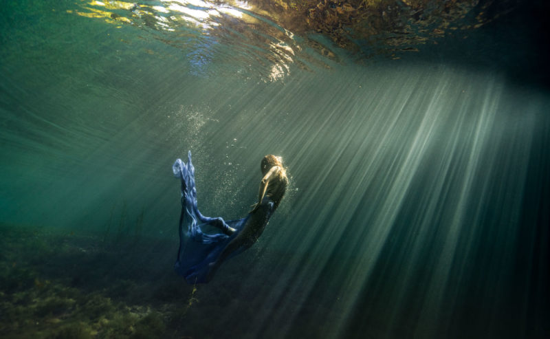 femme sous l'eau dans un bassin naturel sur l'île de La Réunion, lors d'une séance artistique sous l'eau. Elle est entourée des rayons du soleil.